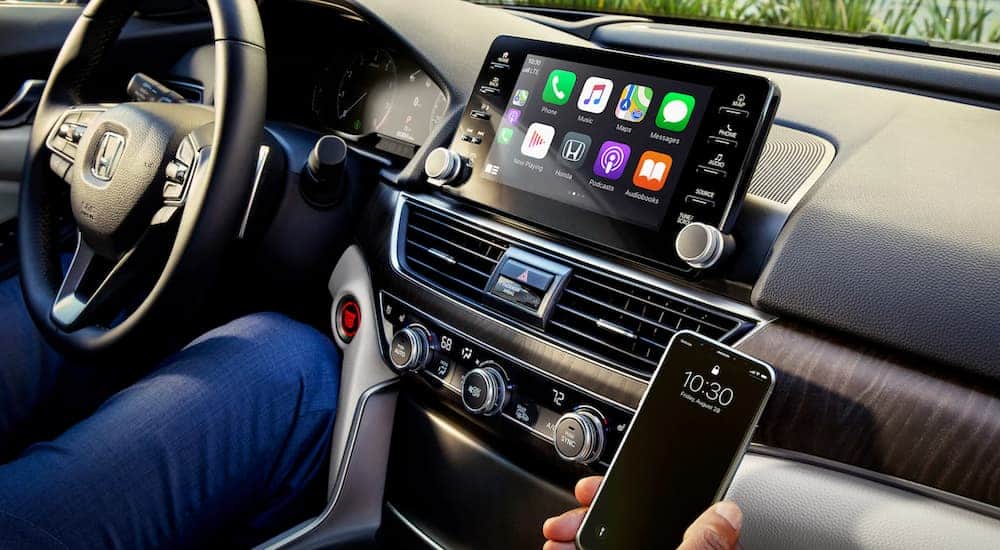 A person is holding a smart phone next to the screen in a 2021 Honda Accord.