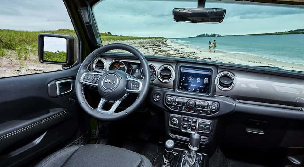 The interior of a 2021 Jeep Wrangler Unlimited shows a beach through the windshield.