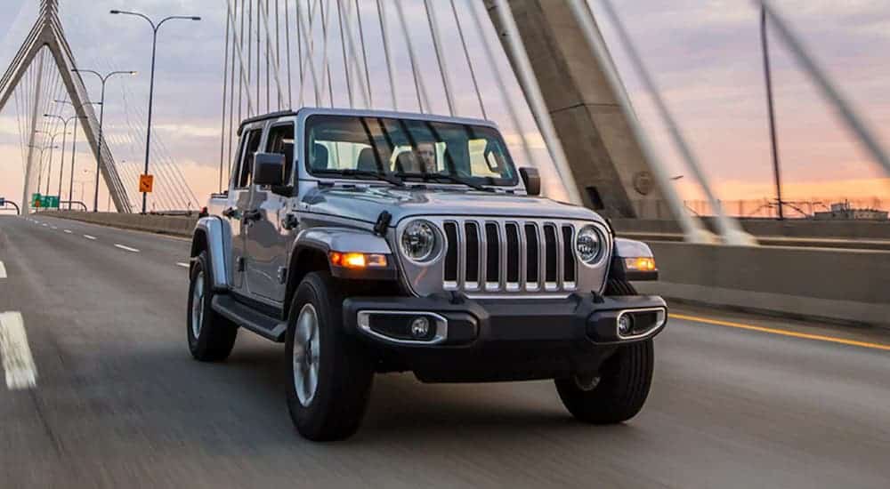 A 2021 Jeep Wrangler Unlimited drives over a bridge at sunset.