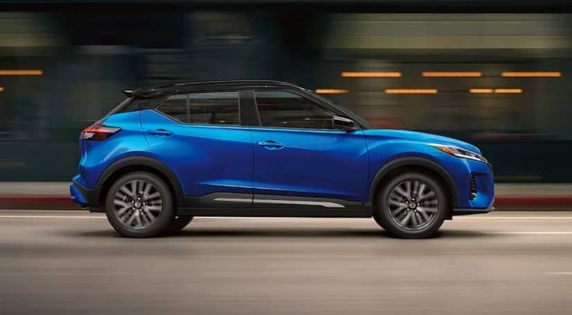 A blue 2021 Nissan Kicks is shown from the side driving through the city.