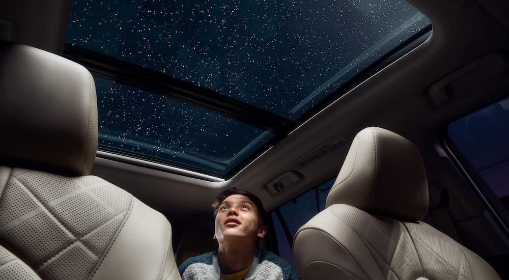 A close up shows a kid from a low angle looking out of the moonroof of a 2021 Toyota Highlander Platinum at a star filled sky.