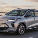 A sliver 2022 Chevy Bolt EUV is driving on a highway at sunset.