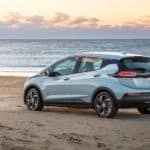 A pale blue 2022 Chevy Bolt EV is parked on a beach and shown from a rear angle.