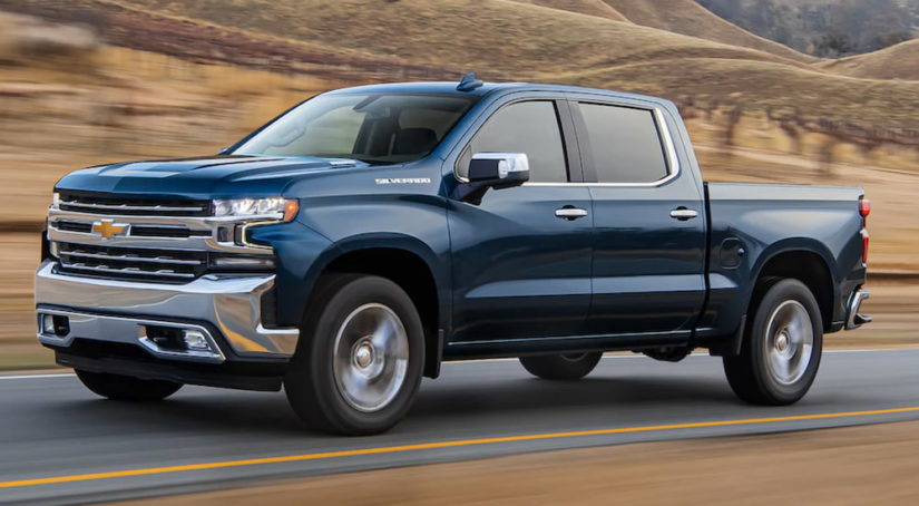 A blue 2021 Chevy Silverado is shown from the side driving past a vineyard after leaving a Chevy dealer.