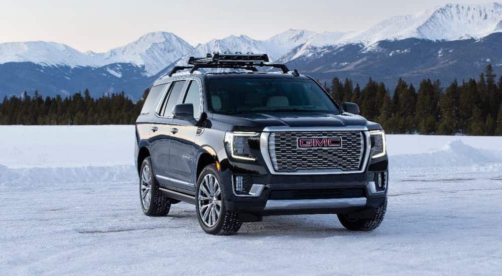 A black 2021 GMC Yukon Denali is parked in front of snow-covered mountains.