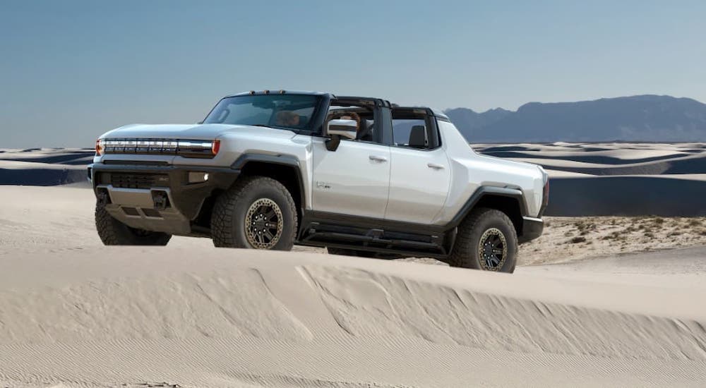 A white 2022 GMC Hummer with no roof is driving on sand dunes.