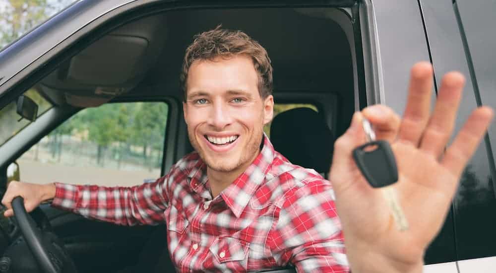 A man in red flannel is smiling and holding up a key for a pickup truck.