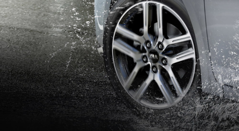 A white 2021 Kia Forte shows a close up of a tire splashing through rain.