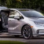 A silver 2020 used Honda Odyssey is shown from the side parked next to a family.