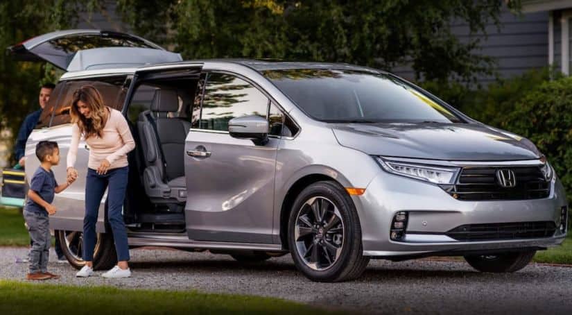 A silver 2020 used Honda Odyssey is shown from the side parked next to a family.