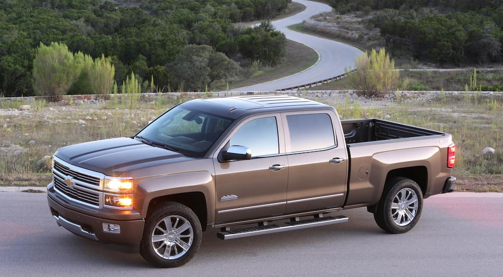 A brown 2015 Chevy Silverado is parked on pavement overlooking a winding road.