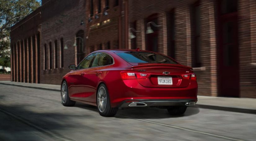 A used red 2020 Chevy Malibu is parked outside of a brick building after leaving a used car dealership.