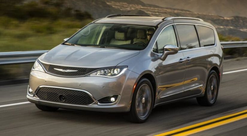 A grey 2017 Chrysler Pacifica is driving down a two way road as the perfect used family car.