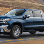 A blue 2020 Chevy Silverado is shown from the side driving down an open road after leaving a used truck dealer.