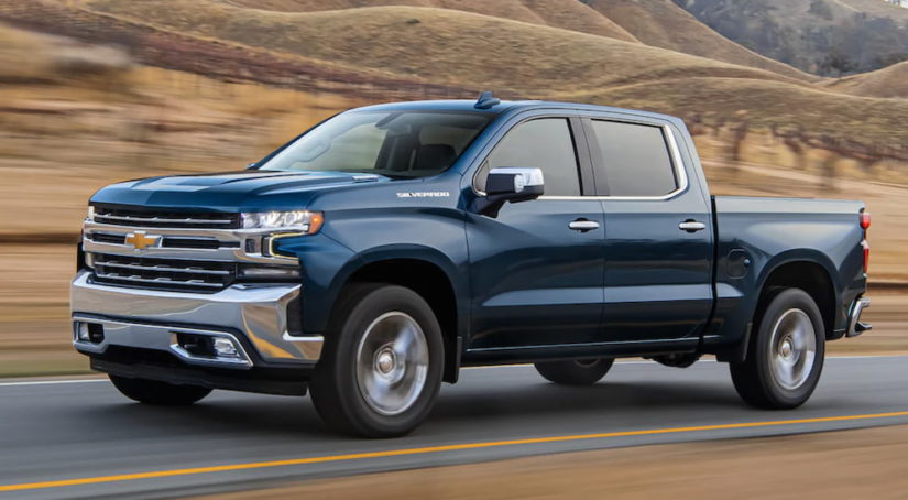 A blue 2020 Chevy Silverado is shown from the side driving down an open road after leaving a used truck dealer.