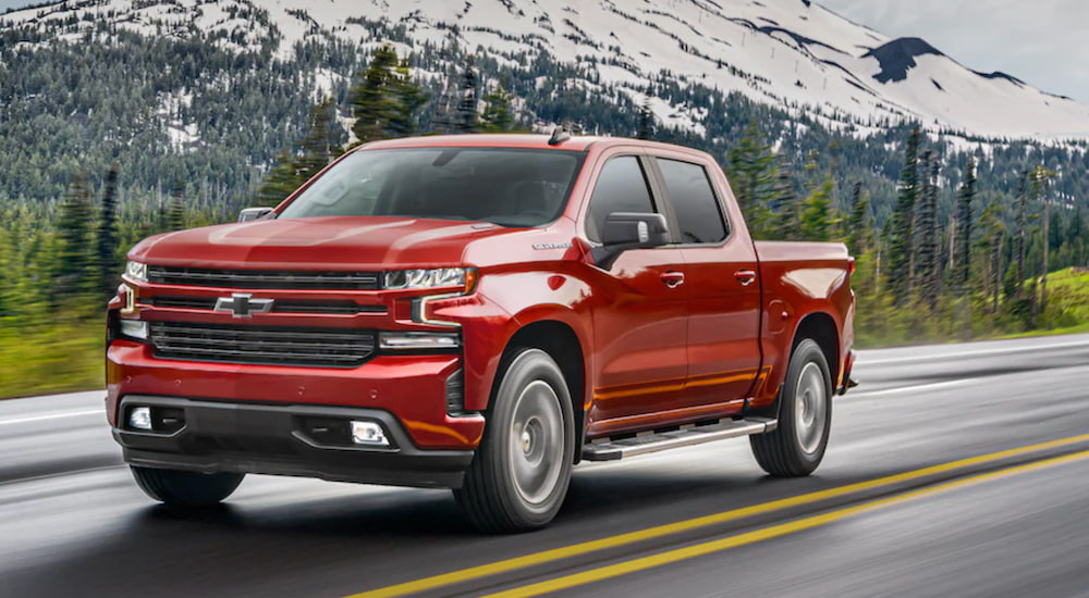 A red 2020 Chevy Silverado is driving on an open road past mountains.