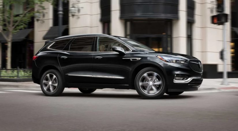 A black 2021 Buick Enclave is shown from the side driving in a city.