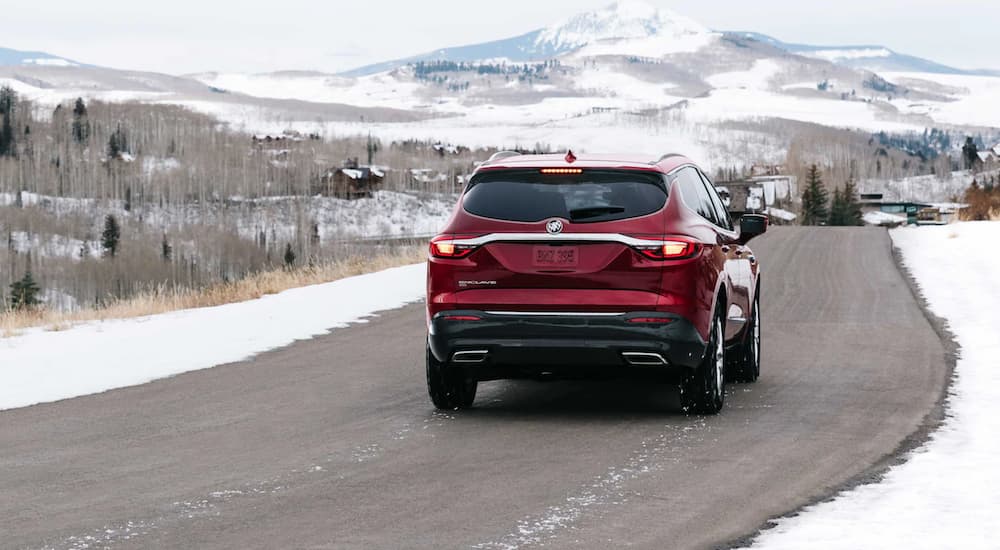 A red 2021 Buick Enclave is shown from the back driving past a snowy mountain.