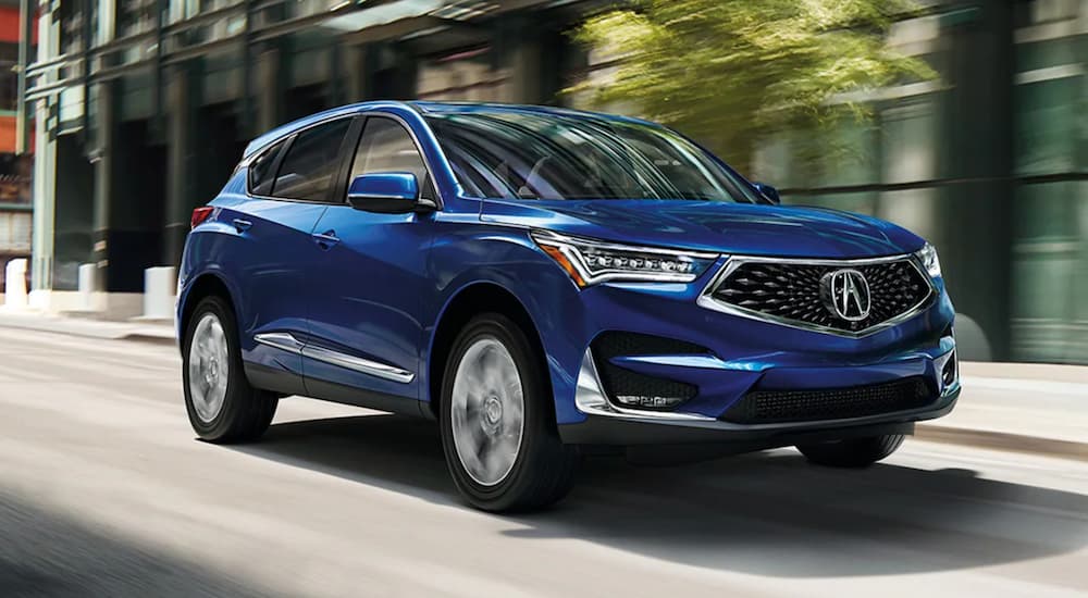 A blue 2021 Acura RDX is driving on a city street.