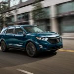 A turquoise 2021 Chevy Equinox is driving through a city after winning a 2021 Chevy Equinox vs 2021 Honda CR-V comparison.