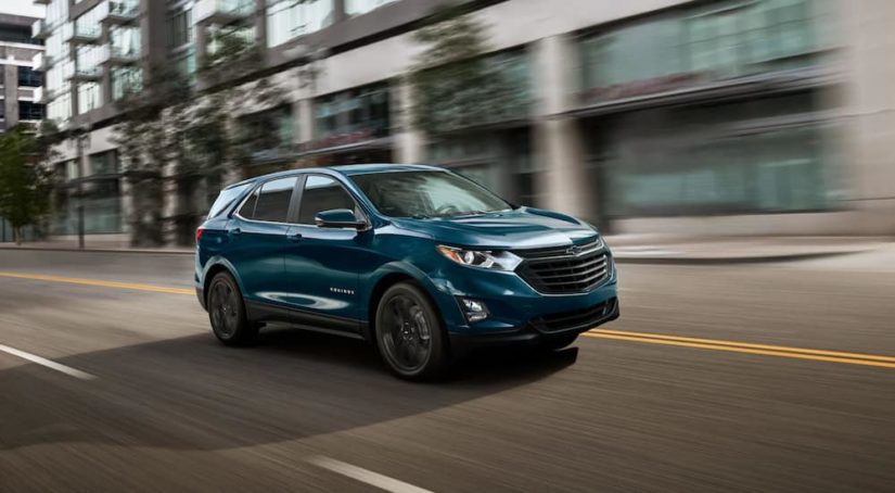 A turquoise 2021 Chevy Equinox is driving through a city after winning a 2021 Chevy Equinox vs 2021 Honda CR-V comparison.