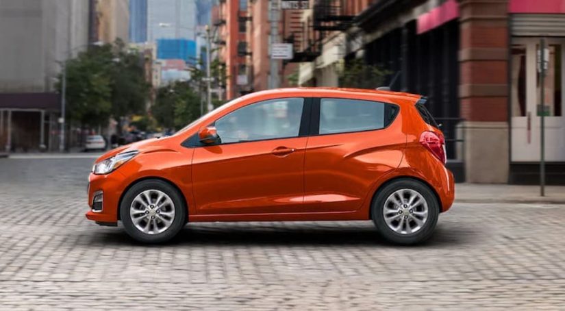 An orange 2021 Chevy Spark is driving through a city after winning a 2021 Chevy Spark vs 2021 Nissan Versa comparison.