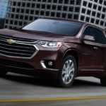 A maroon 2021 Chevy Traverse is shown from an angle driving through a city.