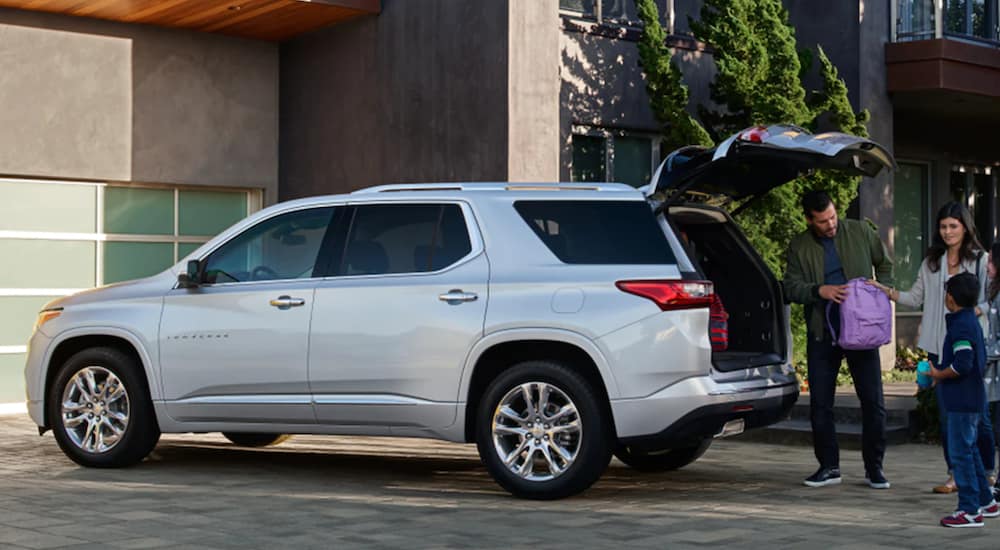 A white 2021 Chevy Traverse is parked in a driveway with the lift gate open as a family loads the car.