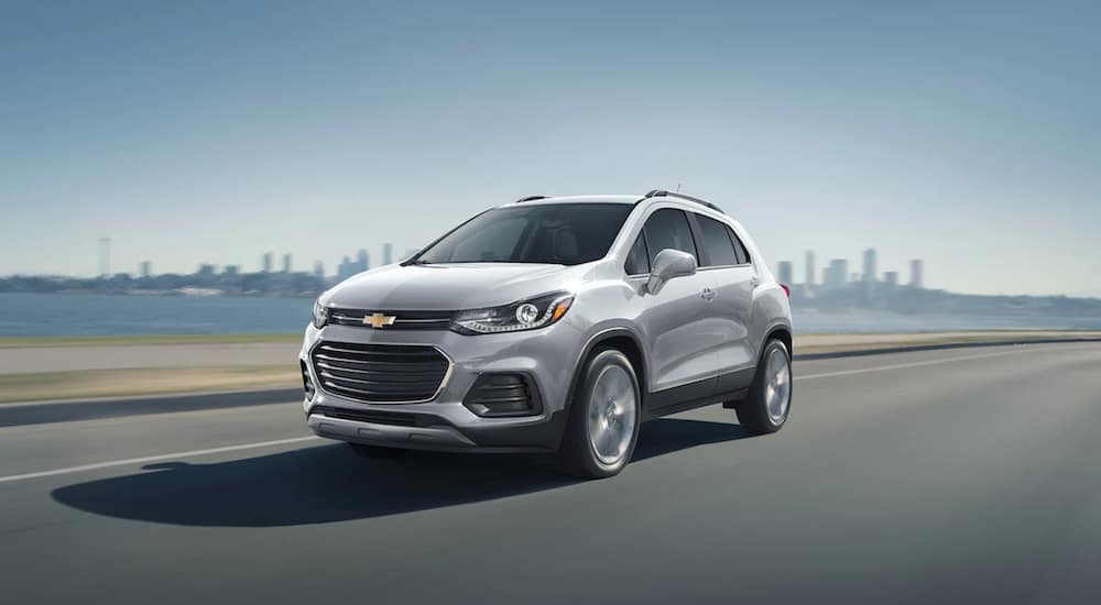 A white 2021 Chevy Trax is shown from an angle driving down an open highway overlooking a bay.