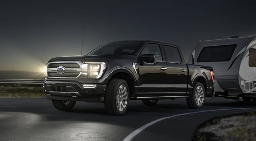 A black 2021 Ford F-150 is towing a camper after winning a 2021 Ford F-150 vs 2021 Ram 1500 comparison.
