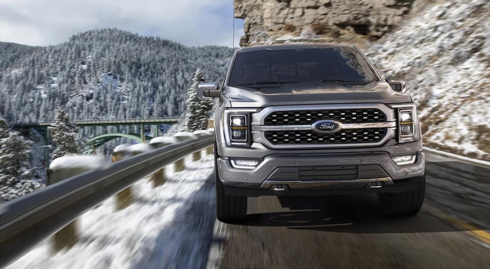 A silver 2021 Ford F-150 is shown from the front driving on a snowy mountain road.