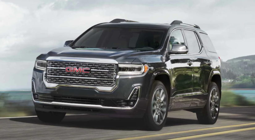 A black 2021 GMC Acadia drives down a two way road after winning a 2021 GMC Acadia vs 2021 Jeep Grand Cherokee comparison.