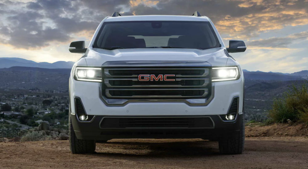 The front of a white 2021 GMC Acadia is shown parked in a dirt clearing.