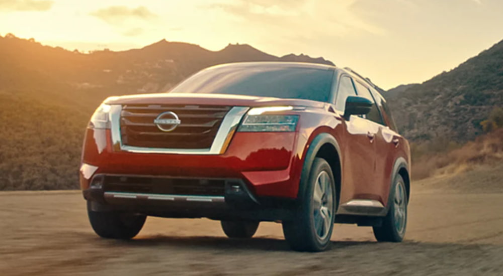 A red 2022 Nissan Pathfinder is driving through the mountains at sunset.