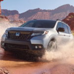 A silver 2021 Honda Passport is driving through a puddle in the desert after winning a 2021 Honda Passport vs 2022 Nissan Pathfinder comparison.