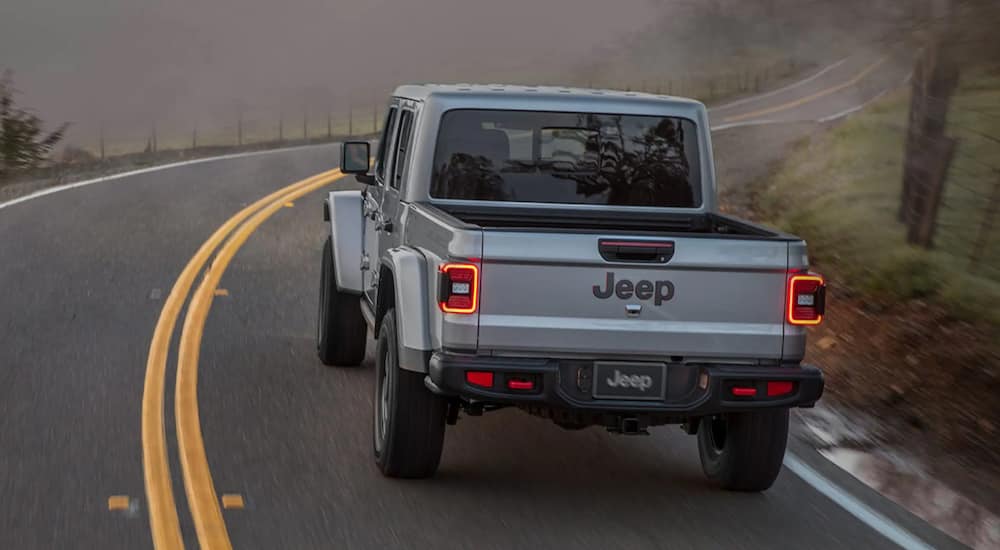 A grey 2021 Jeep Gladiator is shown from the back driving down a winding road.