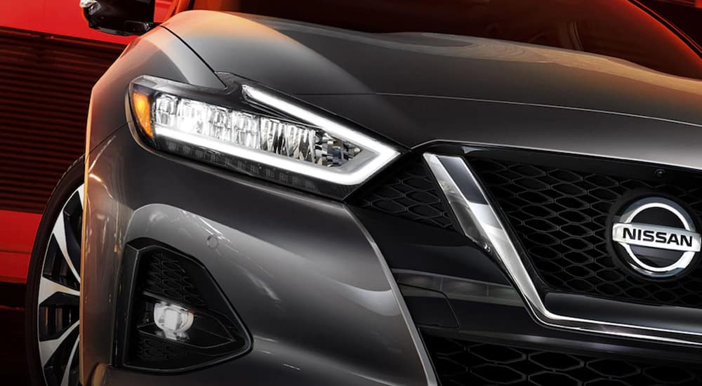 A close up of a silver 2021 Nissan Maxima shows the left headlight and Nissan bowtie.
