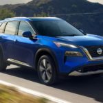 A blue 2021 Nissan Rogue is shown driving on a winding road in the mountains.