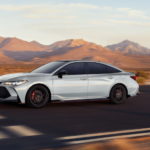 A white 2021 Toyota Avalon is driving on an open road past the desert.