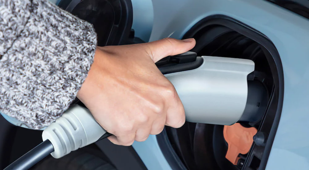 A woman is holding an electric car charger plugged into a 2022 Chevy Bolt EUV.