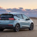 A light blue 2022 Chevy Bolt EV is parked on a beach at sunset.