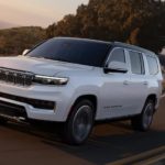 A white 2022 Grand Wagoneer is driving down an open road in front of mountains.