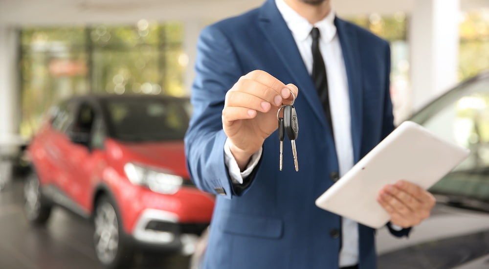 A car salesman holds a set of keys out in front of him.