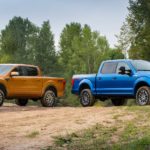 A blue and orange 2019 Certified Pre-Owned Ford F-150 are parked in a dirt field surrounded by forest.