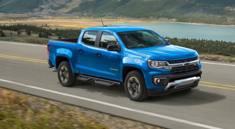 A light blue 2021 Chevy Colorado is driving on a two way road past a body of water after leaving a Chevy Dealer.