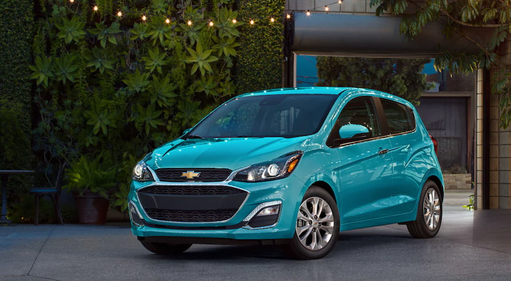 A turquoise 2021 Chevy Spark is parked outside of a house.
