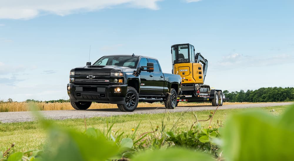 A black 2018 Chevrolet Silverado 2500HD is towing machinery down an open road in farm land as they consider Chevy end of lease details.