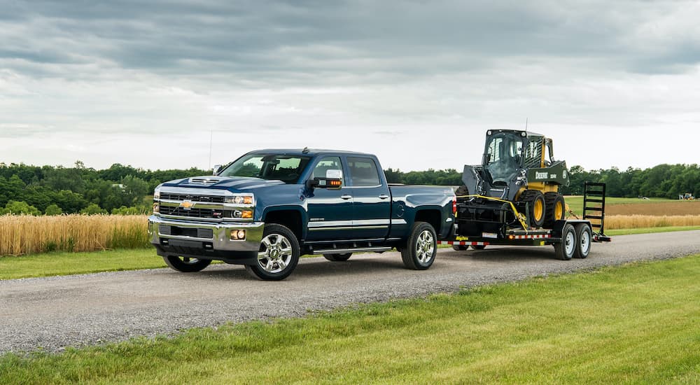 A blue 2018 Chevrolet Silverado 2500HD is towing machinery on a dirt road in the country.