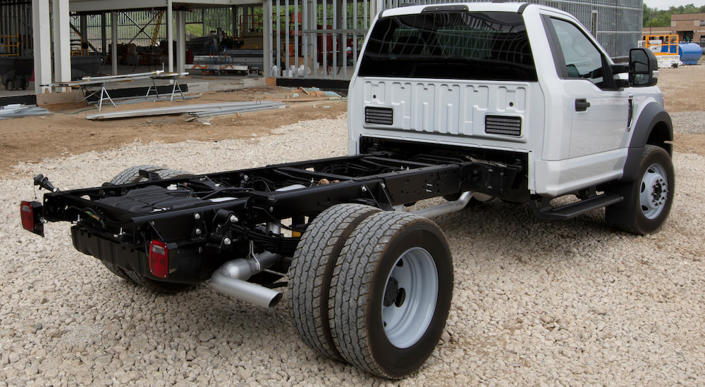 A white 2021 Ford F-600 Chassis is parked on gravel in front of a building. 