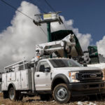 A white 2021 Ford Diesel Truck F-600 Chassis Cab is parked on a mountain in front of a ski lift.